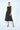 Woman wearing a black sleeveless dress with oversized pockets on a white background
