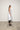 A female model wearing a spaghetti straps white peplum dress with strokes paint design on the side, pockets, low neck line, asymmetrical hem, paired with Black leggings, black sandals against an industrial white background.