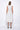 A woman wearing a light grey sleeveless knee-length dress with pockets in a white background setting.