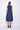 A woman wearing a navy blue sleeveless knee-length dress with pockets in a white background setting.