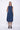 A woman wearing a navy blue  sleeveless knee-length dress with pockets in a white background setting.
