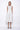 A woman wearing a light grey  sleeveless knee-length dress with pockets in a white background setting.