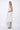 A woman wearing a light grey sleeveless knee-length dress with pockets in a white background setting.