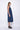 A woman wearing a navy blue sleeveless knee-length dress with pockets in a white background setting.