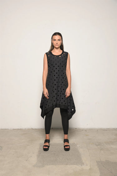 Woman wearing a black sleeveless dress with a polka dot pattern on a plain background