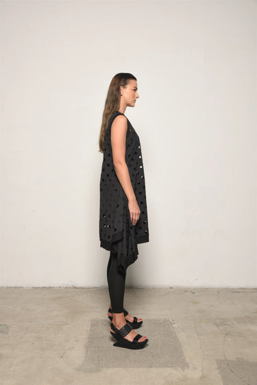 Woman wearing a black dress with cut-out patterns against a white wall.