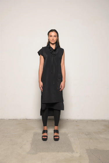 Person wearing a black sleeveless dress with a hood against a plain background