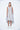 A female model wearing a sleeveless knee-length dress with horizontal black stripes and round neckline, standing against a white background.