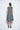 A female model wearing a linen gray sleeveless knee-length dress with vertical stripes and round neckline, standing against a white background.
