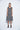 A female model wearing a linen gray sleeveless knee-length dress with vertical stripes and round neckline, standing against a white background.
