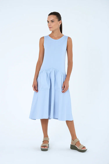 Woman wearing a light blue dress with oversized pockets on a white background