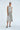 Woman wearing a light gray sleeveless dress with oversized pockets on a white background
