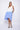 A female model wearing a sleeveless, hand-dyed blue and white knee-length dress with side seam pockets and a racerback design.