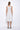 A woman wearing a light grey sleeveless knee-length dress with pockets in a white background setting.