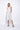 A woman wearing a light grey  sleeveless knee-length dress with pockets in a white background setting.