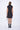 A woman wearing a black sleeveless mini dress with a high collar, pockets and front zipper.