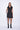 A woman wearing a black sleeveless mini dress with a high collar, pockets and front zipper.