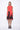 A model wearing a sleeveless, red dress with a black abstract design at the bottom. The dress is knee-length and the model is wearing black sandals.