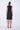 A model wearing a black sleeveless knee-length dress with a v-neckline, elastic at the waist and pockets, standing against a white background.