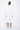 A female model wearing a white long sleeve top and white cropped pants, with white background