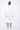 A female model wearing a white long sleeve top and white cropped pants, with white background