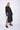 A female model wearing a black long sleeve top and black cropped pants, with white background