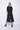 A female model wearing black pants and a matching black top, standing against a white background.