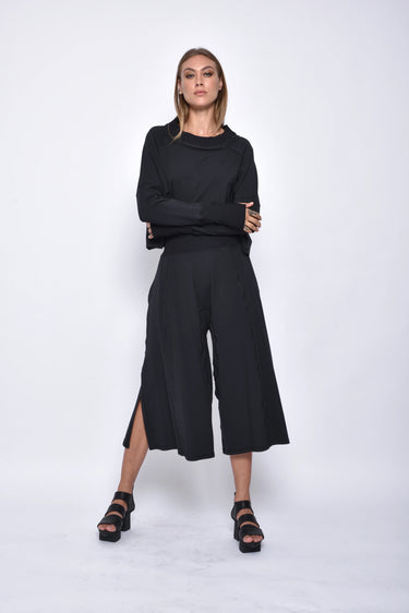 A female model wearing black pants and a matching black top, standing against a white background.