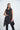 A woman modeling a sleeveless black tunic with a draped cowl neck and Asymmetrical hem, paired with black leggings.