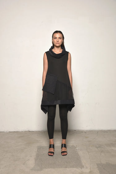 A woman modeling a sleeveless black tunic with a draped cowl neck and Asymmetrical hem, paired with black leggings.