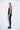 A female model wearing a Black sleeveless top, uneven hem, Black leggings and Black sandals against a white background
