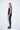 A female model wearing a Black sleeveless top, uneven hem, Black leggings and Black sandals against a white background