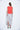 A female model wearing a Red sleeveless top, uneven hem, Black horizontal striped asymmetrical skirt and sandals against a white background
