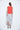 A female model wearing a Red sleeveless top, uneven hem, Black horizontal striped asymmetrical skirt and sandals against a white background