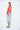 A female model wearing a Red sleeveless top, uneven hem, Black horizontal striped asymmetrical skirt and sandals against a white background