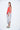 A female model wearing a Red sleeveless top, uneven hem, Black horizontal striped asymmetrical skirt and sandals against a white background