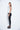 A female model wearing a Light grey sleeveless top, uneven hem, Black leggings and Black sandals against a white background
