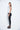 A female model wearing a Light grey sleeveless top, uneven hem, Black leggings and Black sandals against a white background
