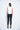 A female model wearing a White sleeveless top, uneven hem, Black leggings and Black sandals against a white background