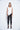 A female model wearing a White sleeveless top, uneven hem, Black leggings and Black sandals against a white background