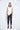 A female model wearing a White sleeveless top, uneven hem, Black leggings and Black sandals against a white background