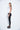 A female model wearing a White sleeveless top, uneven hem, Black leggings and Black sandals against a white background