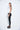 A female model wearing a White sleeveless top, uneven hem, Black leggings and Black sandals against a white background
