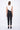 A female model wearing a Black and white sleeveless top, uneven hem, Black leggings and Black sandals against a white background