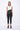 A female model wearing a Black and white sleeveless top, uneven hem, Black leggings and Black sandals against a white background