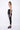 A female model wearing a Black and white sleeveless top, uneven hem, Black leggings and Black sandals against a white background