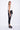 A female model wearing a Black and white sleeveless top, uneven hem, Black leggings and Black sandals against a white background