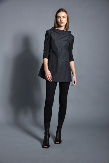 A woman modeling a black top with 3/4 sleeves and textured pattern, paired with black leggings and black boots against a gray background
