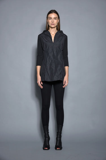 A woman modeling a black top with 3/4 sleeves and textured pattern, paired with black leggings and black boots against a gray background