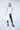 A model wearing an asymmetrical white vest with no sleeves, paired with black pants and black sandals.